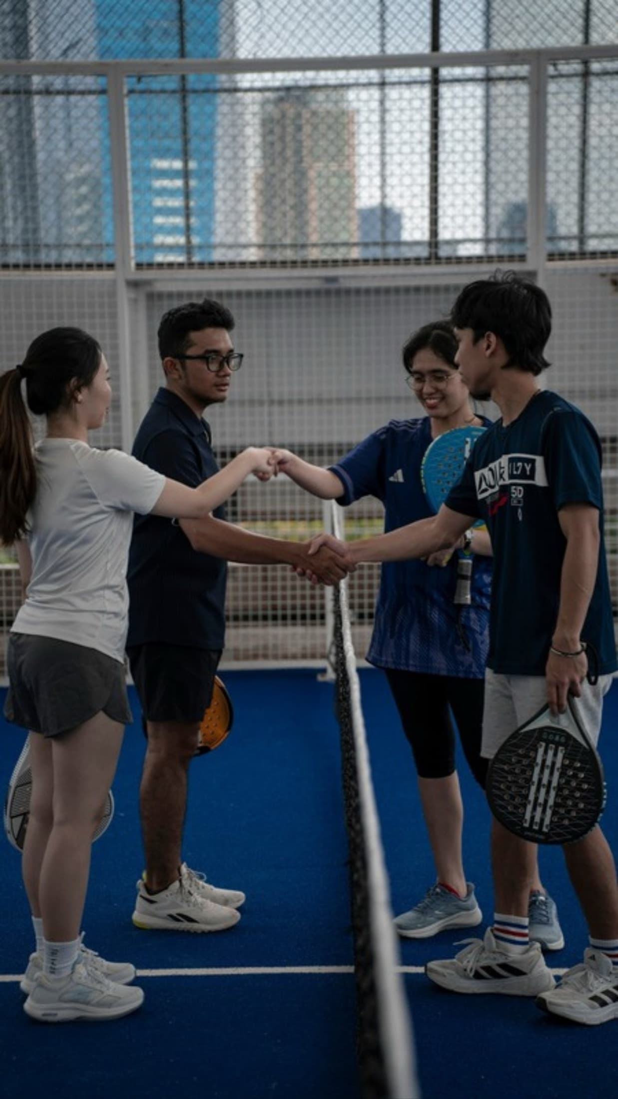 Four padel players shaking hands at the net after a match